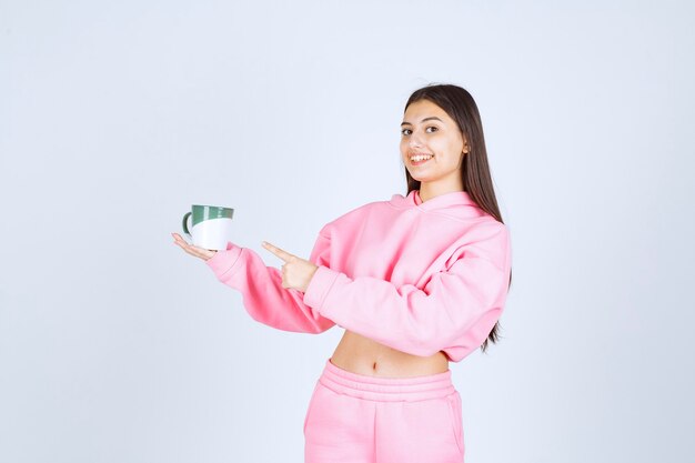 Ragazza in pigiama rosa che tiene una tazza di caffè e che si sente felice.