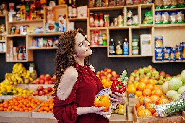 Ragazza in rosso che tiene diverse verdure sul negozio di frutta