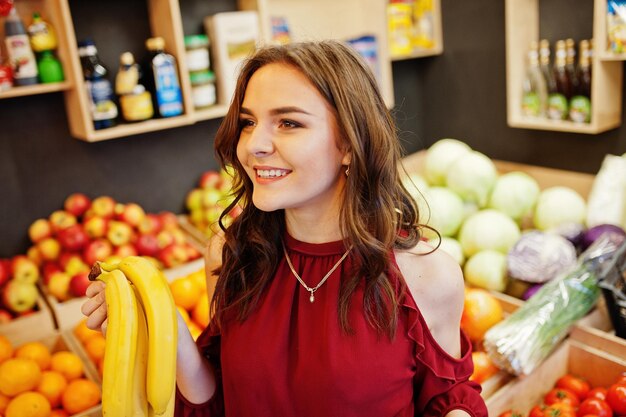 Ragazza in rosso che tiene le banane sul negozio di frutta