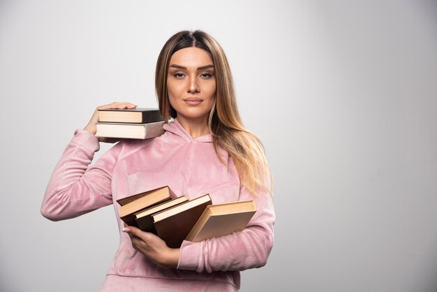 Ragazza in swaetshirt rosa che tiene i suoi libri sopra la sua spalla.