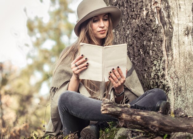 ragazza in un cappello che legge un libro nella foresta di autunno