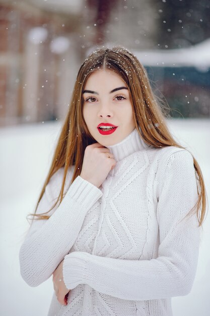 Ragazza in un maglione bianco che sta in un parco di inverno