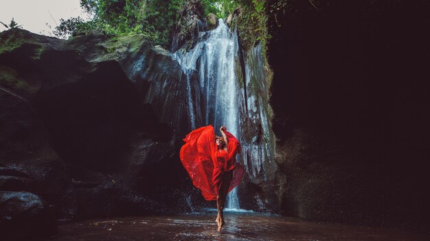 Ragazza in un vestito rosso che balla in una cascata.