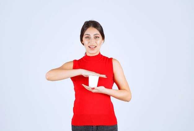 Ragazza in una camicia rossa che tiene una tazza di caffè bianco tra le mani.