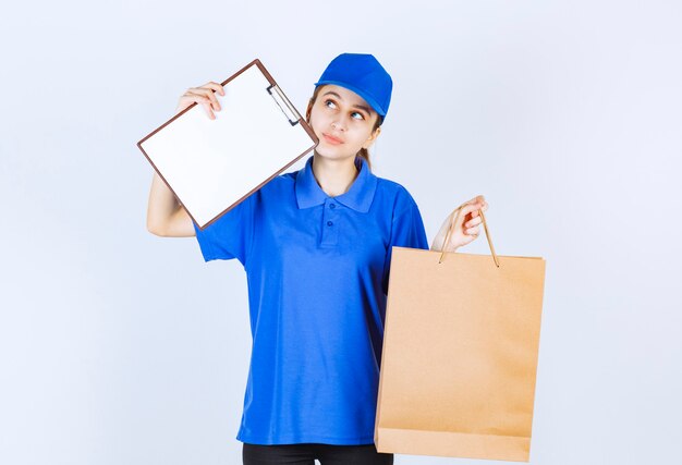 Ragazza in uniforme blu che tiene un sacchetto della spesa del cartone e un elenco di clienti.