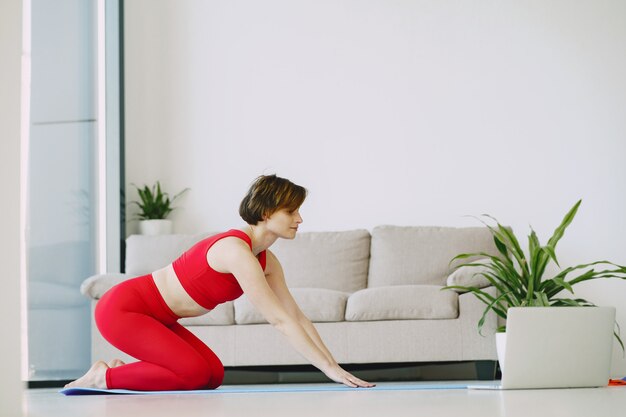 Ragazza in uniforme sportiva rossa praticando yoga a casa