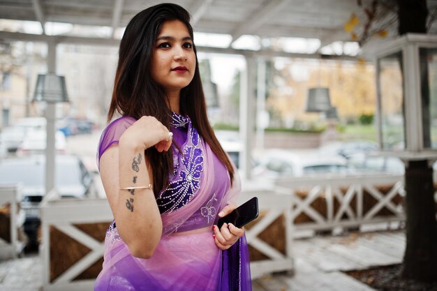 Ragazza indù indiana al tradizionale saree viola poste in strada contro la terrazza in legno