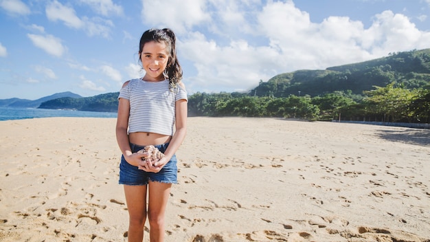 Ragazza inocente con una conchiglia sulla spiaggia