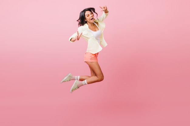 Ragazza latina sensuale sportiva agitando le mani durante il salto. Modello femminile attraente in abiti casual