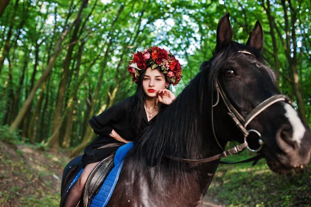 Ragazza mistica in ghirlanda indossata in nero a cavallo in legno