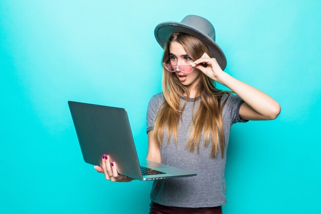 Ragazza modello studente imbarazzato in abiti casual moda funziona orologi sul suo computer portatile isolato su verde