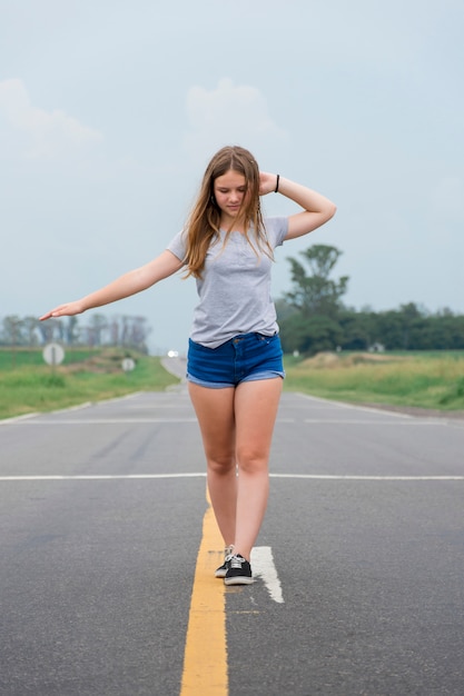 Ragazza moderna adolescente attraente che balla sulla strada vuota