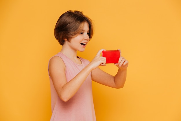 Ragazza moderna felice che per mezzo dello smartphone per la registrazione del video isolata