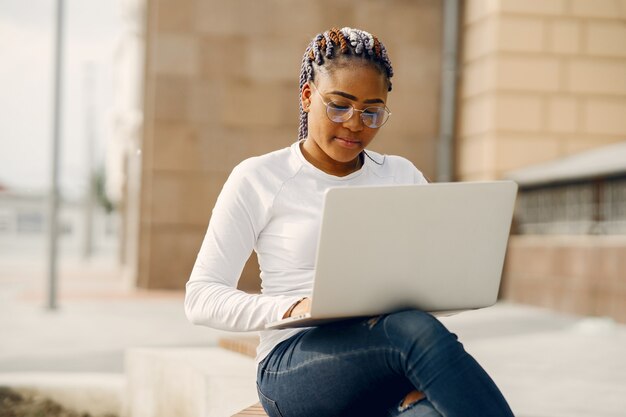 Ragazza nera in una città estiva con il laptop