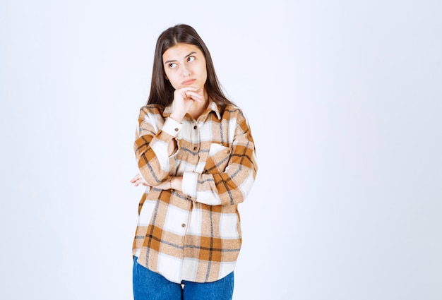 ragazza pensierosa in piedi e in posa sul muro bianco-grigio.