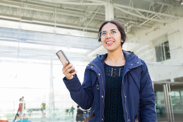 Ragazza positiva sorridente che per mezzo del telefono all&#39;aperto