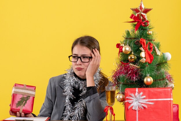 Ragazza premurosa di vista frontale con gli occhiali che si siedono al cocktail dei regali e dell'albero di Natale della tavola