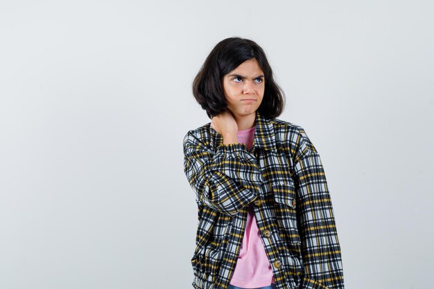 Ragazza preteen in camicia, giacca che si massaggia il collo mentre guarda da parte e sembra turbata, vista frontale.