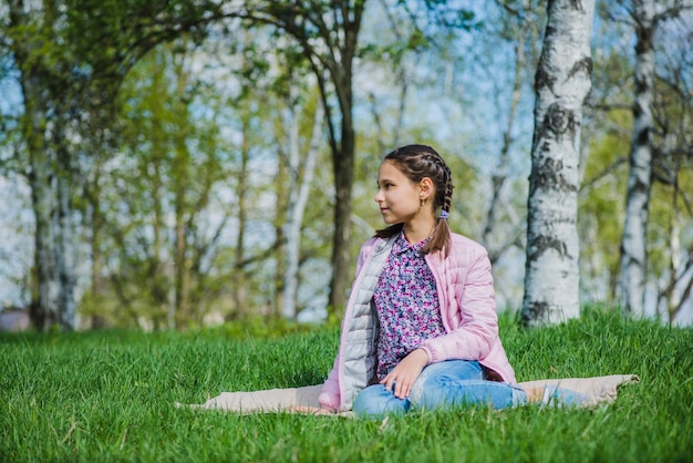 Ragazza rilassata seduta sull&#39;erba e guardando al fianco