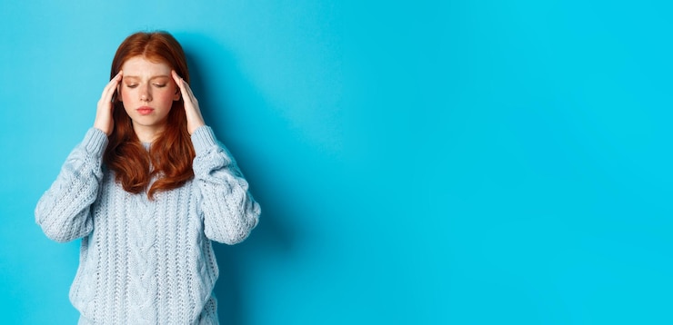 Foto gratuito ragazza rossa adolescente in difficoltà che tocca la testa guardando in basso con l'espressione del viso travagliata in piedi ag
