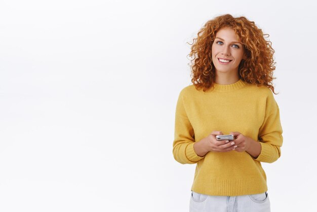 Ragazza rossa allegra e attraente con i capelli ricci che utilizza l'app di carsharing ordina un taxi con l'applicazione per smartphone tieni il telefono cellulare sorridente soddisfatto e felice di messaggiare o navigare sui social media