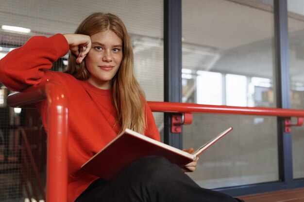 Ragazza rossa attraente intelligente, uno studente adolescente che studia nella sala della biblioteca, leggendo un libro.