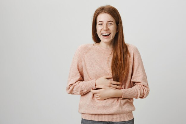 Ragazza rossa che ride ad alta voce, tocca la pancia come una risatina