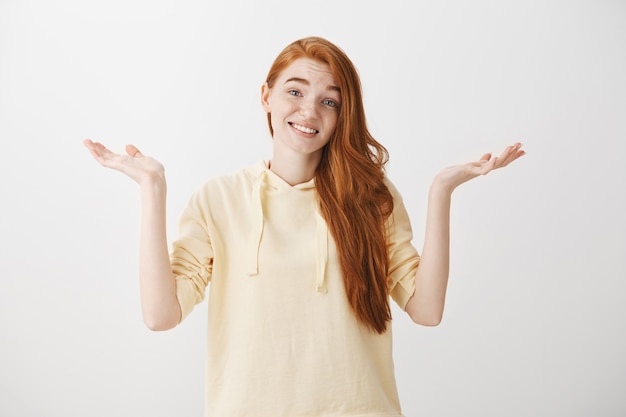 Ragazza rossa confusa indecisa che scrolla le spalle con un sorriso forzato