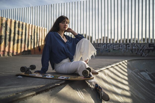 Ragazza seduta accanto a uno skateboard in uno skate park