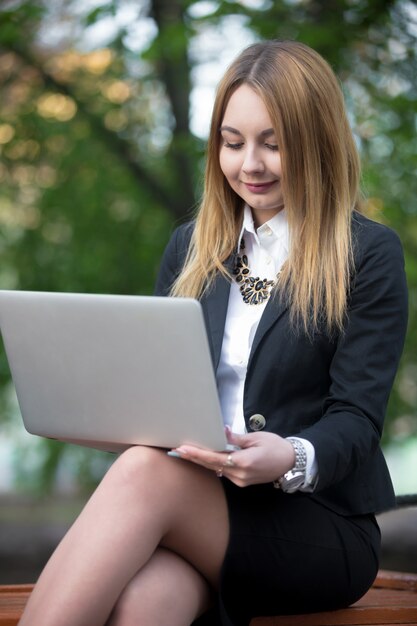 Ragazza seduta con il computer portatile sulla panchina