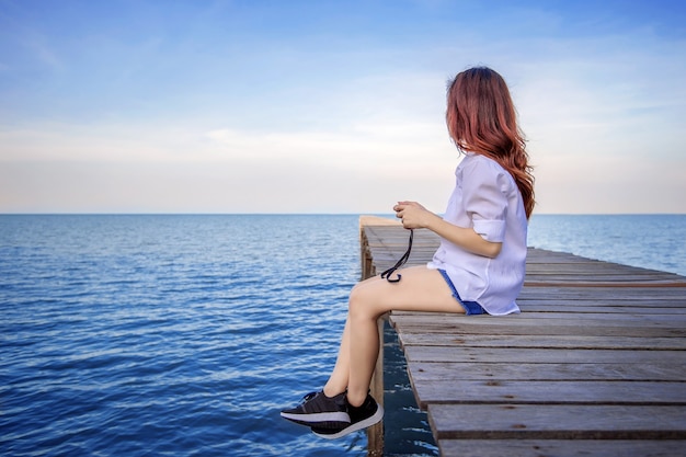 Ragazza seduta da sola su un ponte di legno sul mare. Stile vintage.
