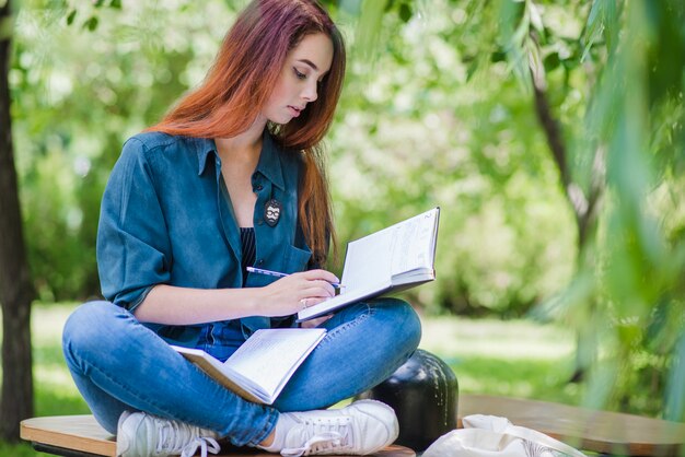 Ragazza seduta in parco sulla lettura della tabella