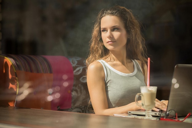 Ragazza sexy con i capelli lunghi che lavora con diversi contratti. Libero professionista seduto al ristorante con una tazza di caffè con latte.