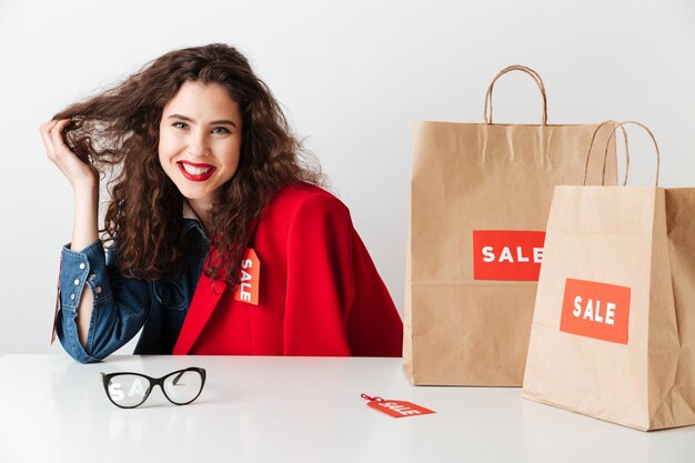 Ragazza shopaholic sorridente che si siede con i sacchetti della spesa di carta