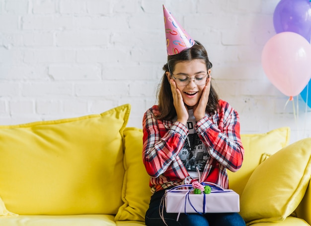 Ragazza sorpresa che si siede sul sofà con il regalo di compleanno