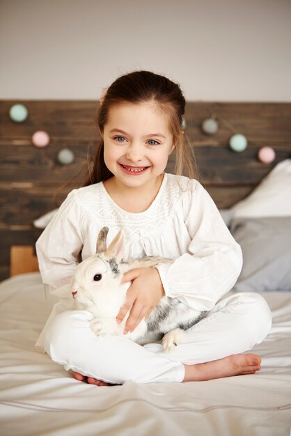Ragazza sorridente che abbraccia il suo coniglio a letto