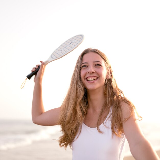 Ragazza sorridente che gioca a tennis in spiaggia