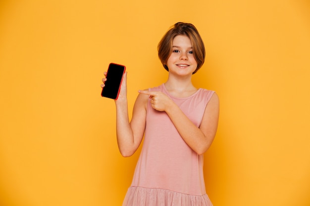 Ragazza sorridente che indica allo schermo in bianco dello smartphone isolato