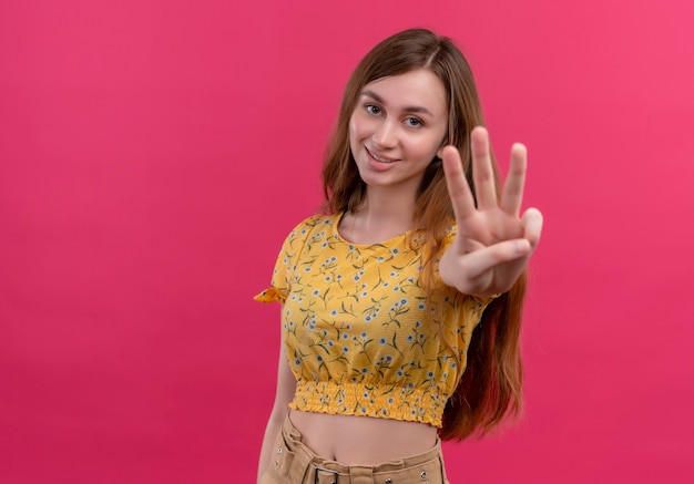 Ragazza sorridente che mostra tre sulla parete rosa isolata con lo spazio della copia