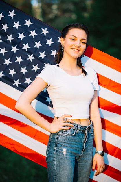 Ragazza sorridente che posa davanti alla bandiera americana in natura