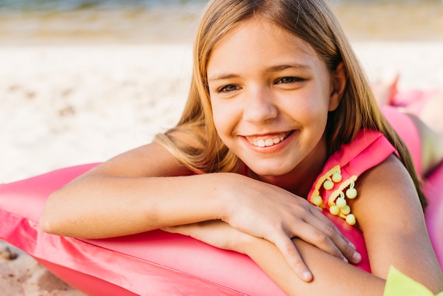 Ragazza sorridente che riposa sul materasso di aria sulla spiaggia