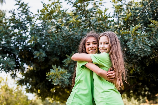 Ragazza sorridente che si abbracciano contro l&#39;albero verde