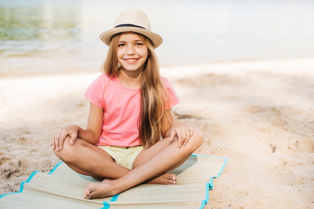 Ragazza sorridente che si siede alla spiaggia