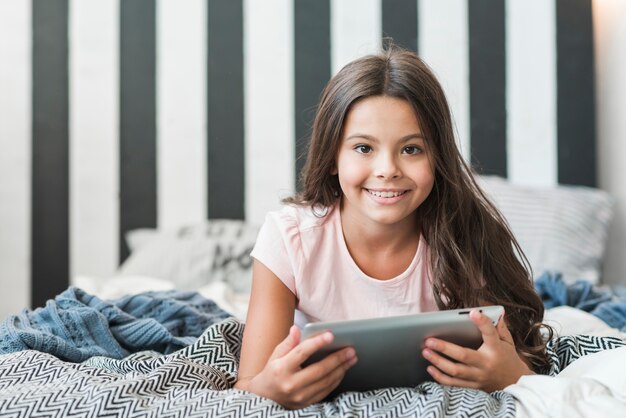 Ragazza sorridente che si trova sul letto sudicio con tavoletta digitale