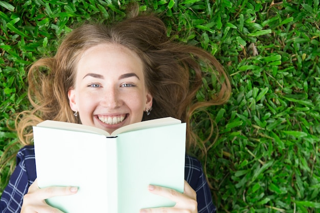 Ragazza sorridente che si trova sull&#39;erba e sul libro di lettura