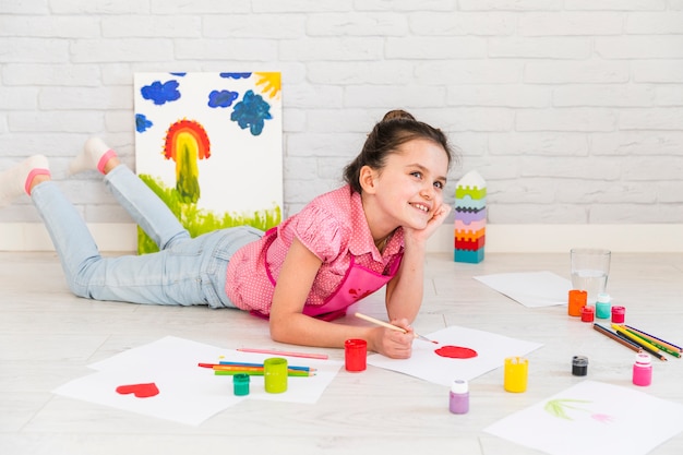 Ragazza sorridente che si trova sulla pittura del pavimento sul Libro Bianco con la spazzola rossa