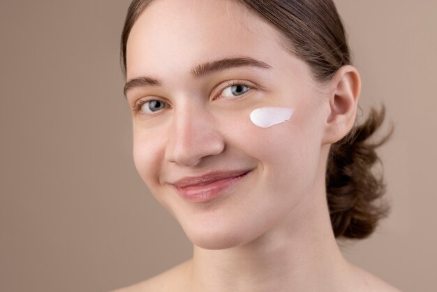 Ragazza sorridente che utilizza la vista laterale della crema per gli occhi