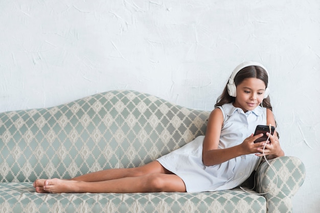 Ragazza sorridente con la cuffia sulla sua testa guardando il telefono cellulare