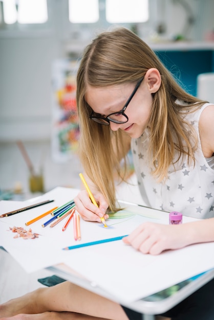 Ragazza sorridente con la pittura della matita su carta al tavolo nella sala