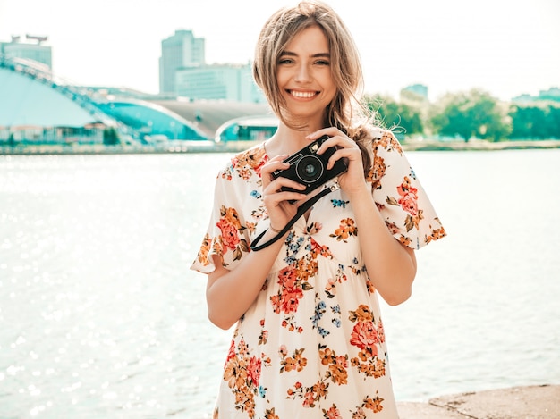 ragazza sorridente dei pantaloni a vita bassa in prendisole estivi d'avanguardia che tengono retro macchina fotografica